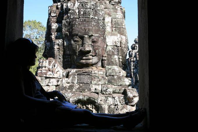 Lesen im Schatten vor dem Stein Gesicht, Bayon, Angkor Thom, Angkor, Kambodscha
