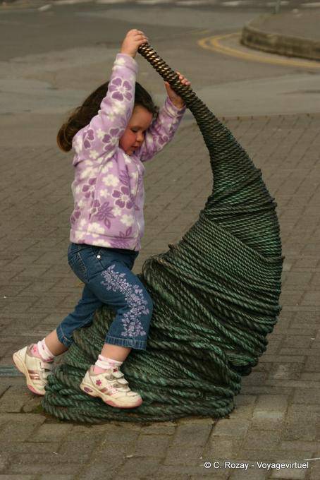 Kleines Mädchen, das auf einer Skulptur, Dingle - Irland
